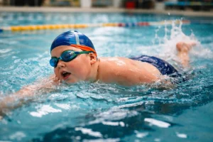 Gyermek úszás közben egy fedett uszodában, miközben a helyes légzésre koncentrál.